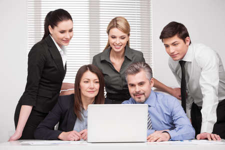 Large group of people looking together at laptop. Smiling and searching something, discussing ideasの写真素材