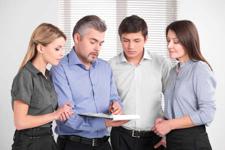 Handsome adult business man showing something on documents. Standing together in bright modern officeの写真素材