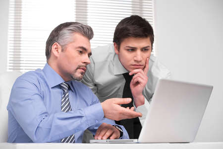 Thoughtful young business man looking at laptop. Adult middle aged durector asking adviceの写真素材