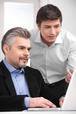 Young businessman showing his boss something on laptop. Close up of two business men working in modern officeの写真素材