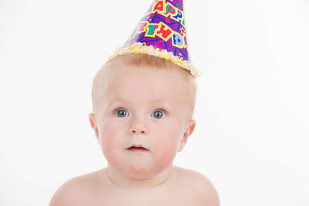 Portrait of cute funny baby in birthday party hat. Looking at camera isolated over white backgroundの写真素材