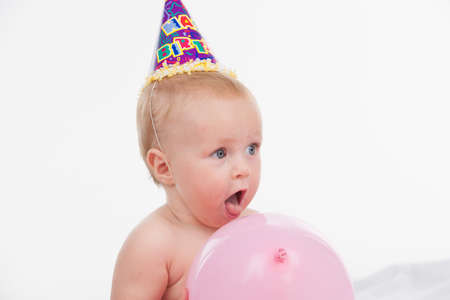 Close up of Cut little baby with pink balloon. Standing in party hat isolated over white backgroundの写真素材