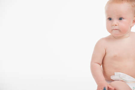 Cute little baby looking away at empty white space. Sitting in diapers isolated over white backgroundの写真素材