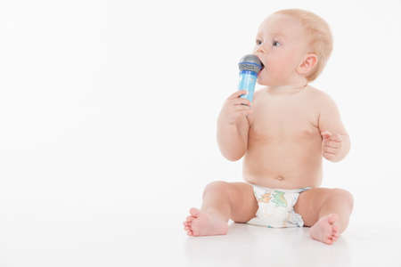 Little funny baby holding microphone and looking at copy space. While sitting isolated over white backgroundの写真素材