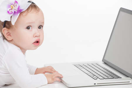 Close up of Cute little baby with flower posing with laptop. Laying isolated over white backgroundの写真素材