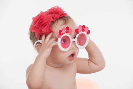 Portrait of Funny little baby girl in funny party glasses. Sitting and looking away with surprise...