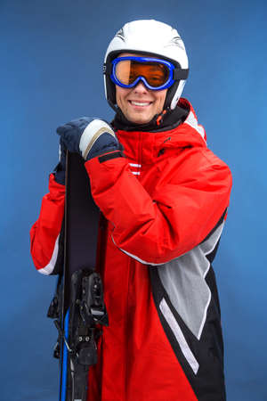 Portrait of smiling attractive male skier. Standing with ski isolated over blue backgroundの写真素材