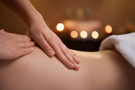 gentle hand massage of girl back. burning candles on background near sinkの写真素材