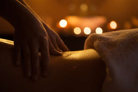 hand massage of back with oil  burning candles on background near sinkの写真素材