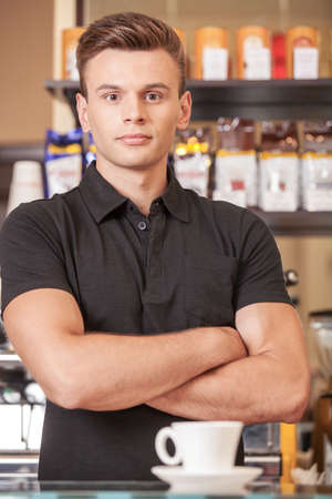 serious young barista behind counter. handsome young man and cup of coffeeの写真素材