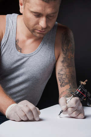 young tattooist drawing picture on paper. young man looking at ink gun の写真素材