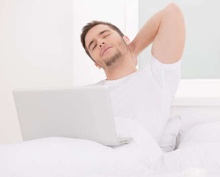 handsome man sitting in bed and working. Attractive young male surfing internetの写真素材