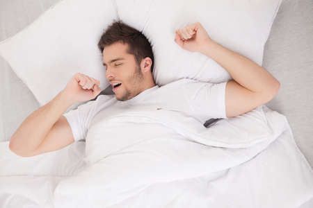 young attractive man waking in morning. handsome guy stretching and yawning in bedの写真素材
