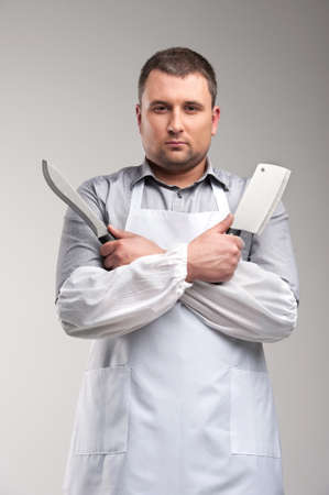 young butcher standing and looking serious. man holding two butcher knivesの写真素材