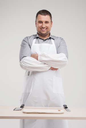 smiling butcher standing behind table. professional butcher and two knives on tableの写真素材