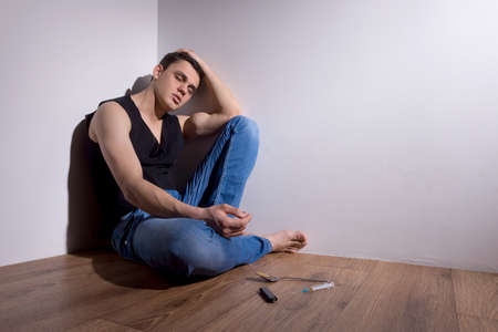 young man sitting in corner with needle. handsome guy in jeans closed eyesの写真素材