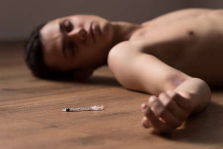 young handsome dude lying on floor. man sleeping by used needle after shotの写真素材