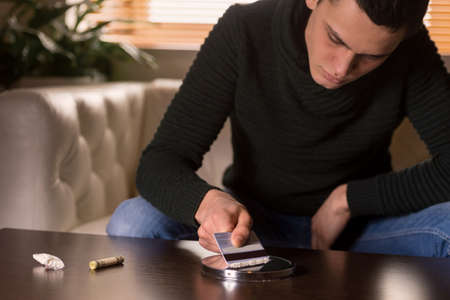 handsome man spreading cocaine on mirror. young guy holding credit cardの写真素材