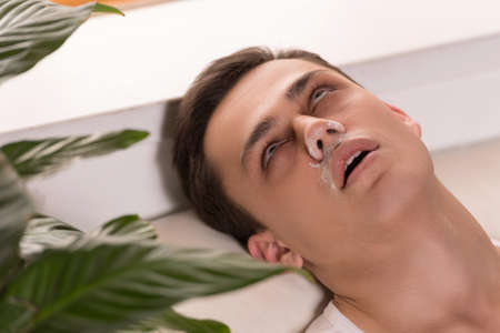 young man lying on white couch. drug addict passed out and became unconscious