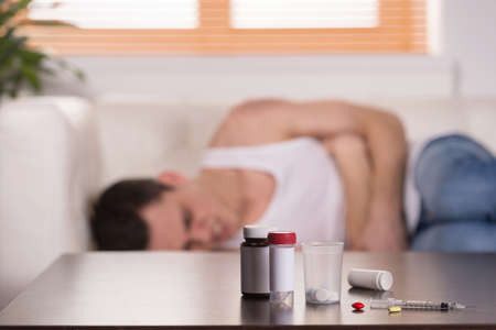 young man lying on couch in pain. drug addict experiencing pain from pillsの写真素材