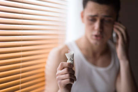 young handsome man holding drugs. upset drug addict talking on phone の写真素材