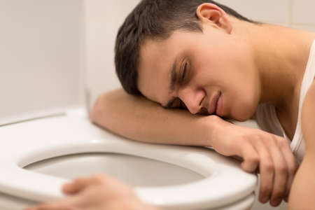 young man lying on toilet seat. drug addict kneeling over toilet seatの写真素材