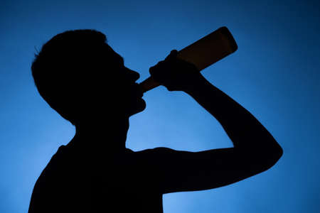 young man drinking alcohol from bottle. young drunkard holding bottle and standingの写真素材