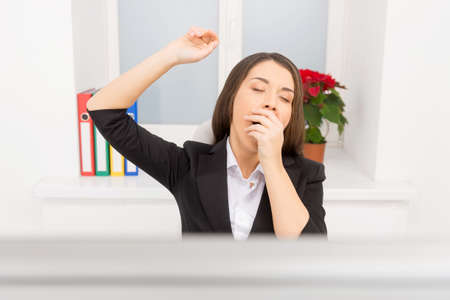 young girl sitting at work and yawning. beautiful brunette sitting tired at work の写真素材