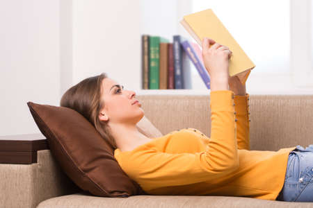Beautiful young woman reading book. attractive girl lying on sofa at home の写真素材