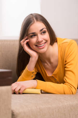 beautiful girl lying on brown sofa. young woman closeup image with bookの写真素材