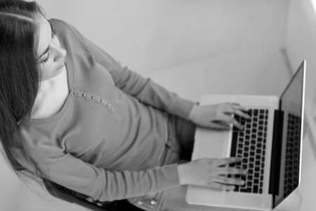 Young woman sitting on chair and checking email. black and white picture of girl working on computerの写真素材