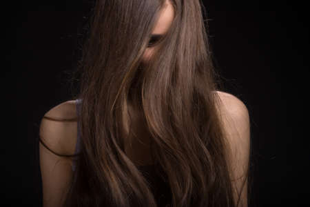 beautiful brunette girl standing on black background. closeup portrait of girl long hair の写真素材