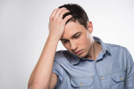 handsome young man holding head. attractive male standing in confusion and contemplationの写真素材