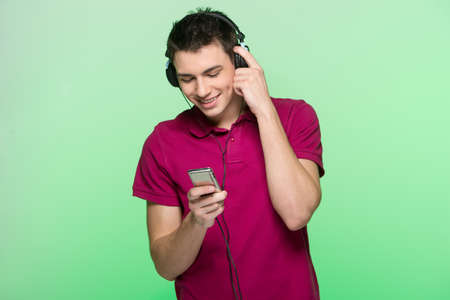 handsome young man standing and listening music. Attractive male holding headphones and playerの写真素材