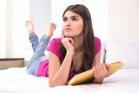 beautiful serious girl reading book. pretty girl lying on bed and looking upの写真素材