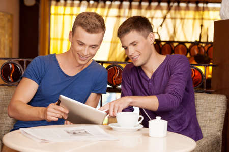 two young guys talking in cafe. handsome man holding tablet and listeningの写真素材