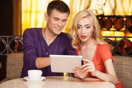 beautiful girl sitting in cafe surprised. handsome guy smiling and showing on screenの写真素材
