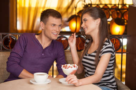beautiful couple sitting in cafe and eating. brunette girl giving ice-cream to manの写真素材