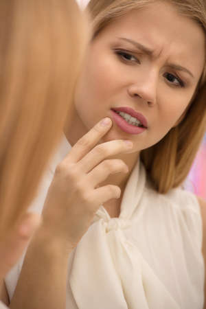 beautiful young woman looking into mirror. attractive blond girl touch acneの写真素材