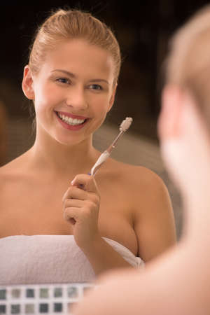 smiling young girl holding toothbrush. beautiful blond looking into mirror and smilingの写真素材