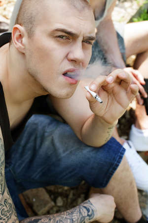 dangerous gangster sitting outside and smoking. closeup of criminal with tattoo looking into cameraの写真素材