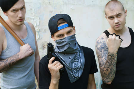 three gangsters with weapons looking into camera. criminals holding baseball bat, gun and knucklesの写真素材