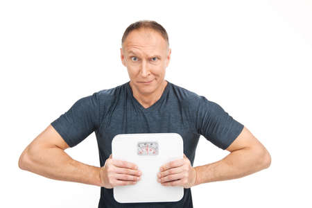 disappointed aged man squeezing scales. upset male holding weight scales