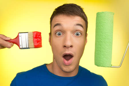 handsome man with paint brush and roller. young guy expressing emotions on yellow backgroundの写真素材