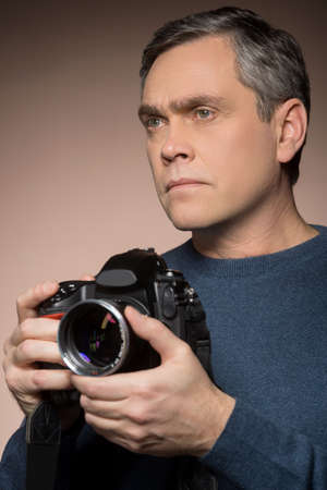 closeup of older man holding camera. portrait of man on brown background taking photos 