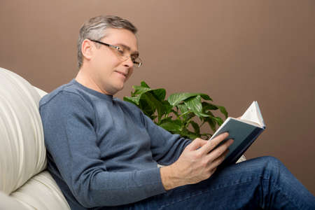 older man reading book on sofa. man sitting on couch and holding book
