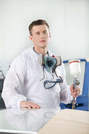 young man standing and holding airbrush. handsome guy in respirator painting car