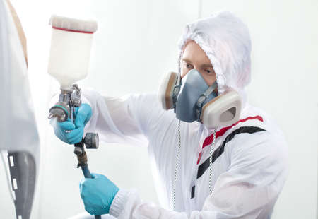 young man painting using airbrush. man wearing respirator and white hood