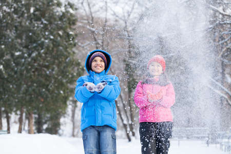 boy and girl throwing snow into air. two children playing in park and smilingの写真素材