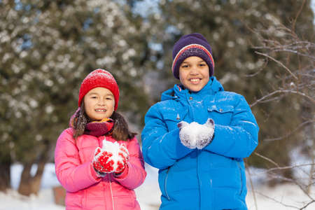boy and girl holding snow and smiling. two children looking into camera in parkの写真素材
